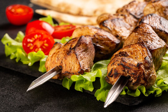 Two portions of shish kebab on a stone plate with salad.