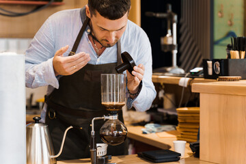 Barista sniffs flavored coffee in syphon device. Barista checks coffee in syphon. Coffee brewing syphon alternative method. Advert for social networks for cafe and restaurant.