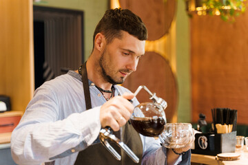 Syphon alternative method of making coffee. Barista pours hot coffee in syphon device for customers. Coffee brewing in cafe. Scandinavian method of coffee making.