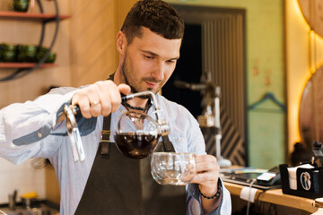 Syphon alternative method of making coffee. Barista pours hot coffee in syphon device for customers. Coffee brewing in cafe. Scandinavian method of coffee making.