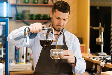 Syphon alternative method of making coffee. Barista pours hot coffee in syphon device for customers. Coffee brewing in cafe. Scandinavian method of coffee making.