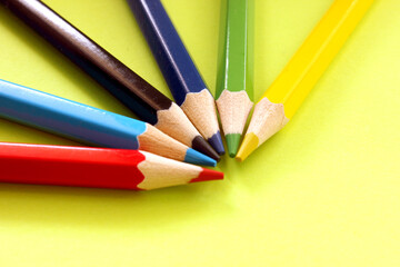 Fototapeta premium Semicircle of colored pencils on a yellow background. Lots of different colored pencils. Colored pencil. Pencils are sharp. Pencils lie in top left corner. Close-up. Copy space. Background. Flat lay