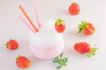 Strawberry milkshake on a light background in a transparent glass. Around - strawberries. The concept of delicious fresh drinks, healthy food for breakfast and snack.