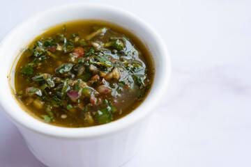 Raw homemade Argentinian green Chimichurri or Chimmichurri salsa or sauce made of parsley, garlic, oregano, hot pepper, olive oil, vinegar, photographed overhead with natural light