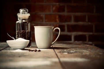Coffee jar with beans next to coffee mug and sugar on a wooden table.