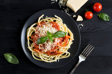 Italian pasta with tomato sauce and parmesan  in the black  plate on the dark wooden background....