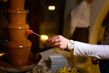 hand with skewer takes piece of apple into chocolate  fondue
