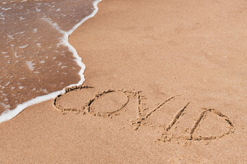 Covid free, stop Covid, safe beach and holiday, word written on the sand with wave washing and cleaning