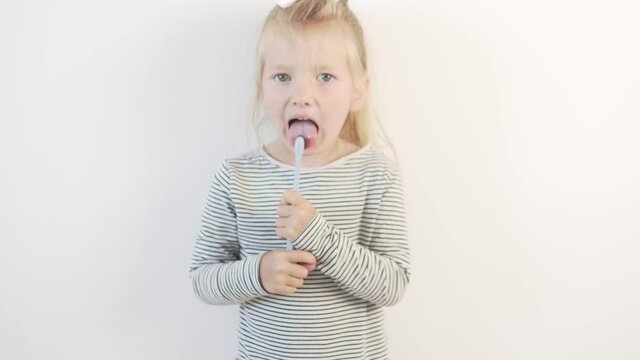 Funny little girl brushes her teeth with a toothbrush on a white background.