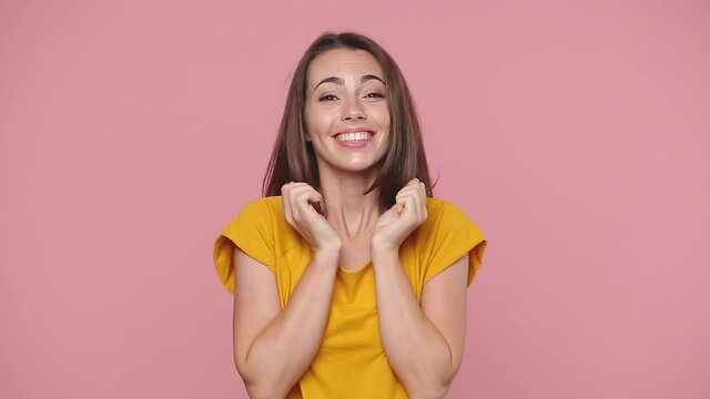 Smiling good kind cute young woman girl 20s years old in yellow t-shirt posing isolated on pastel pink background studio. People lifestyle concept. Look camera say oh it is so sweet put hand on heart