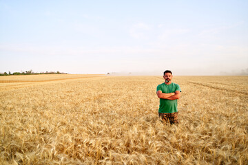 Happy farmer proudly standing in wheat field with arms crossed on chest. Agronomist wearing...