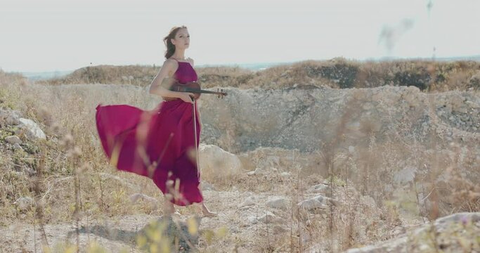 Woman in windy dress and blowing hair stands with violin and bow on white rock