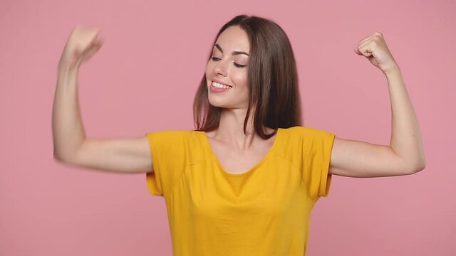 Strong sporty fitness young woman girl 20s years old in yellow t-shirt posing isolated on pastel pink background studio. People lifestyle concept Look camera charming smile showing biceps muscles hand