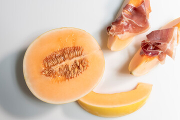 half melon next to some slices with thin cured ham slices on top of them.Tasty food and lifestyle concept.