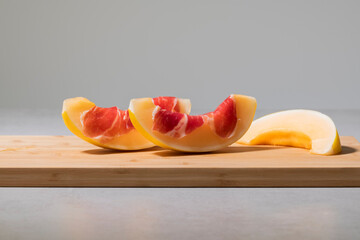 Two delicious looking melon slices with cured ham on top next to another slice on a cutting board