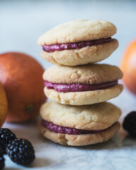 Vertical stack of blood orange blackberry cookie sandwiches with whole blood oranges in background