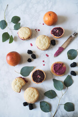 Flatlay of blood orange blackberry cookie sandwiches on marble surface with greenery