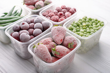Frozen berries and vegetables in plastic boxes on a light background