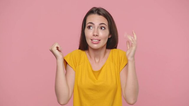 Fun confused shy shamed young woman girl 20s years old in yellow t-shirt posing isolated on pastel pink background studio. People lifestyle concept. Looking camera spreading hands say oops i am sorry
