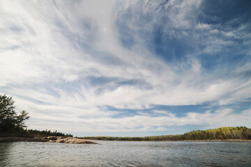 Wide shot of dramatic prairie sky over blue lake surrounded by trees and Canadian shield