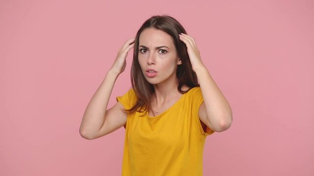 Side view shocked young woman 20s years old in yellow t-shirt turn round look camera put hands on head say ask what isolated on pastel pink background studio. People sincere emotions lifestyle concept