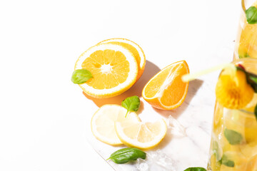 Fototapeta na wymiar Citrus lemonade or mojito cocktail with lemon and orange and basil. Cold beverage or drink with ice on marble cutting board