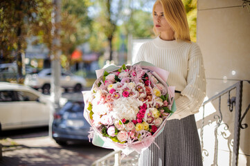 handsome woman in white sweater holds huge bouquet of roses and looks away.