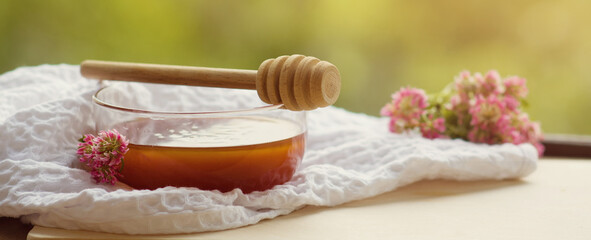 Fototapeta na wymiar Banner Golden transparent honey in a glass bowl with a wooden spoon for honey on a wooden table on a sunny summer day outdoors.