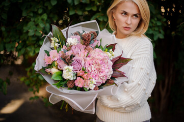 woman in white sweater holds large bouquet of different flowers and looks away.