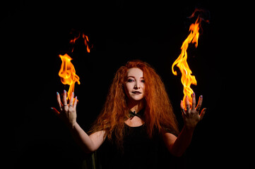 A witch with long curly hair holds a magic fire. Tongues of flame on the palms of a red-haired...