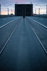 Fototapeta na wymiar a road with rails stretching away into the horizon and a girl standing in the middle of a beautiful sunrise against the backdrop of a drawbridge