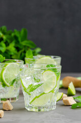 Fresh summer mojito drink with lime slices, mint, ice cubes and brown sugar in a glass on a dark background. Vertical, copy space.