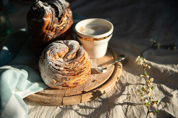Homemade cruffin breads with dried fruits, cocoa and cinnamon fillings on wooden board and blooming cherry twig on linen tablecloth .