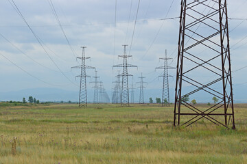 Industrial background of high voltage power lines. Electricity pylons crossing along field.