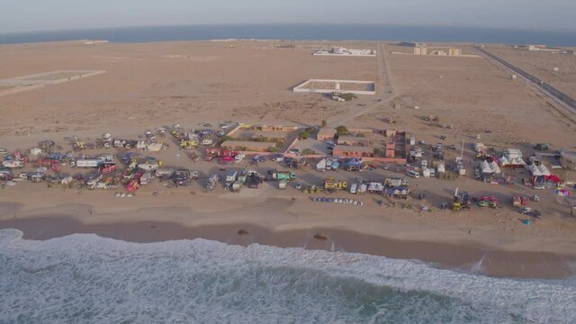 Aerial drone shot of temporary rally car village on the beach of Dakhla, Morocco for the Africa Eco Race or Dakar Rally. Waves lapping on the beach with the desert in the background.