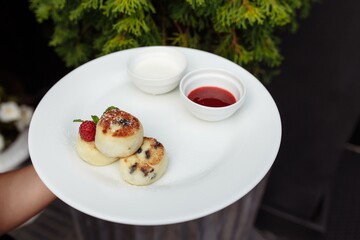 Fresh cheesecakes with berries. Cheesecakes with raspberries and sour cream on a tarek in the waiter's hand