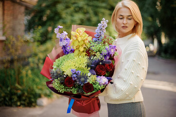 Fototapeta premium young blonde woman in white sweater holds bouquet with different bright flowers