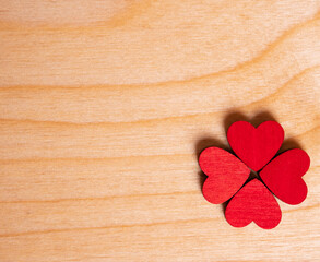 A four-leaf clover made of red hearts is laid out on a wooden background