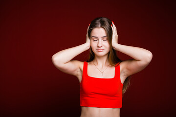 Young woman with long hair and a red T-shirt covered her ears with her hands and looks maliciously to the side