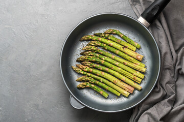 The process of making asparagus in a frying pan. Fresh asparagus in a frying pan on a grey concrete...