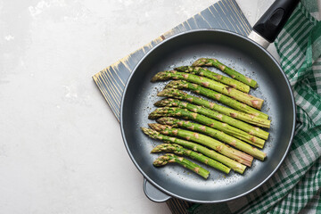 The process of making asparagus in a frying pan. Fresh asparagus in a frying pan on a grey concrete...