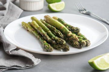 Appetizingly cooked asparagus with pieces of lime on a grey concrete table.
