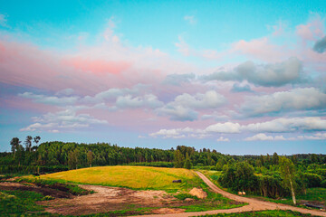 Pink clouds over rural field with trees and lake,  vivid and dramatic landscape.