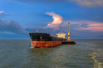 Floating Crane Transhipper for loading Bauxite aluminum ore from the mini bulk carrier (feeder) vessel to the anchored big ocean-going ship at the Kamsar port, Guinea, West Africa.