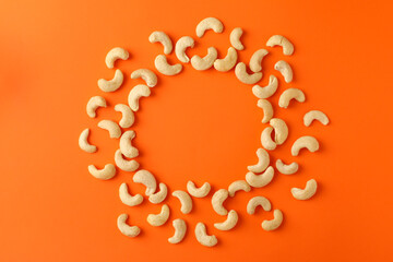 Circle made of cashew nuts on orange background. Vitamin food