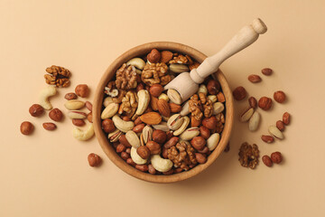 Bowl with different nuts and wooden scoop on beige background
