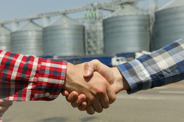 Businessmen shake hands against silos. Agriculture business