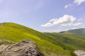 Fototapeta na wymiar Stone against the backdrop of green mountains and serene blue skies