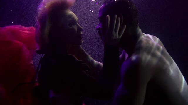 Close-up portrait of a tender couple in love who are under water and look at each other, a buxom girl in a dress and a dark-skinned man. They are on a dark background with bubbles.