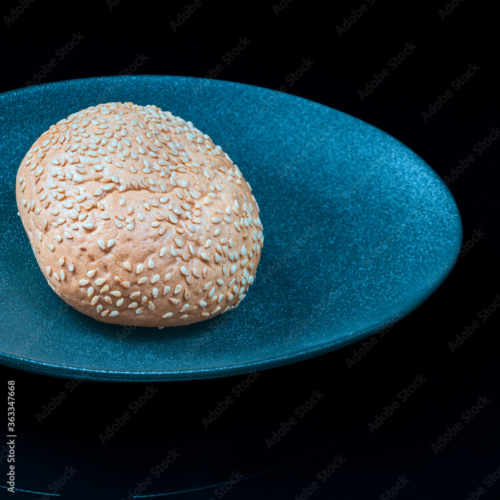 Wall mural fresh wheat bun on a colored plate on a dark background